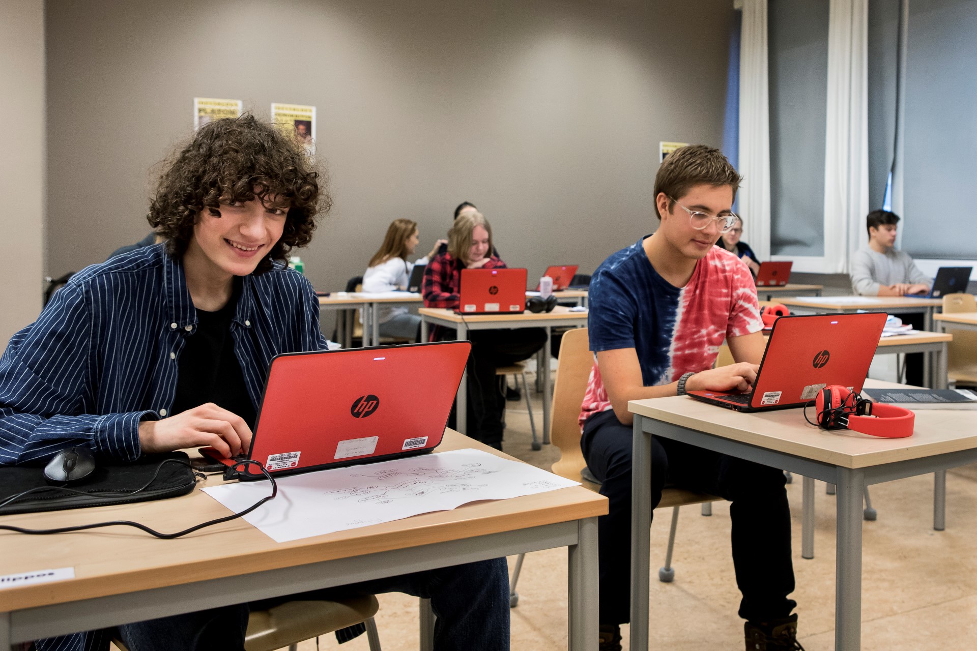 Pojke sitter med dator i klassrum och ler