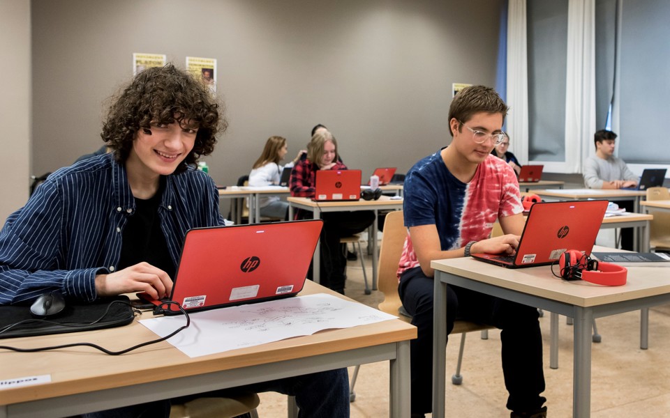 Pojke sitter med dator i klassrum och ler